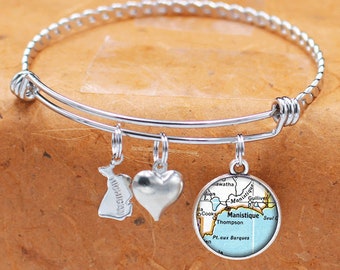 May include: A silver charm bracelet with three charms: a heart, a state of Michigan outline, and a map of Manistique, Michigan.