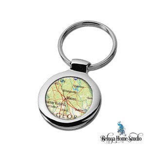 May include: Silver keychain with a round, colorful map of Macon, Georgia. The map shows the city and surrounding areas, including Warner Robins, Milledgeville, and Eatonton. The keychain is a great way to show your pride in your hometown.