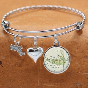 May include: A silver expandable bangle bracelet with three charms: a heart, a silver outline of Massachusetts, and a round charm with a vintage map of Nantucket Island. The map shows the location of Great Pt., Coatue Beach, Nantucket Harbor, Sankaty Hd., and Blascosot.