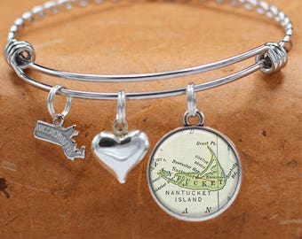 May include: A silver expandable bangle bracelet with three charms: a heart, a silver outline of Massachusetts, and a round charm with a vintage map of Nantucket Island. The map shows the location of Great Pt., Coatue Beach, Nantucket Harbor, Sankaty Hd., and Blascosot.