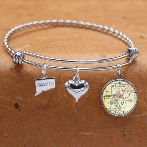 May include: A silver expandable bangle bracelet with three charms: a heart, a state of Connecticut charm, and a round charm with a vintage map of Danbury, Connecticut.