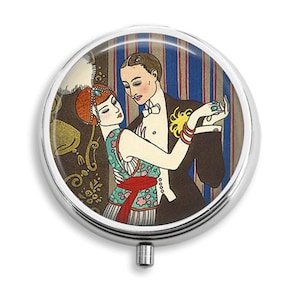 以下が含まれることがあります： 1920年代のアールデコ様式で踊るカップルを描いた、カラフルなイラストが施されたヴィンテージスタイルのコンパクトミラー。女性は緑と赤のドレスに羽根飾りをつけたヘッドピースを着用し、男性は白い蝶ネクタイをつけた黒いタキシードを着用しています。