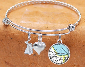 May include: A silver bangle bracelet with three charms: a heart, a state of Michigan outline, and a map of Marquette, Michigan. The map charm is blue, yellow, and green.