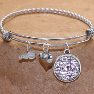 May include: Silver-toned bangle bracelet with three charms. Charms include a Kentucky state outline, a heart, and a round charm with a map of Lexington, Kentucky. The bracelet has a twisted rope design on the top.