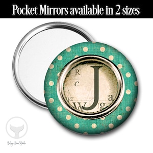May include: A teal blue pocket mirror with white polka dots. The mirror has a silver frame and a vintage-style graphic of the letter "J" in the center. The text "VZ", "R", "C", "W", "g", and "a" are visible around the letter.