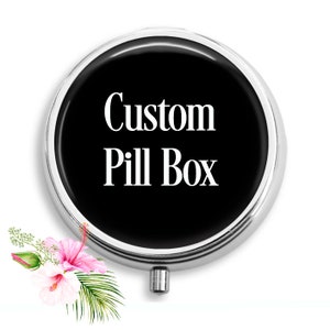 Op de afbeelding: Een ronde, zilveren pillendoos met een zwart deksel. Het deksel heeft de tekst "Custom Pill Box" in wit.