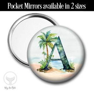 May include: A round pocket mirror with a white background and a watercolor design of a palm tree and the letter A in shades of blue and green. The mirror is available in two sizes.
