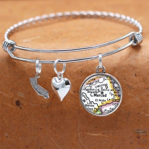 May include: A silver charm bracelet with three charms: a heart, a state of California outline, and a round charm with a map of Merced, California.