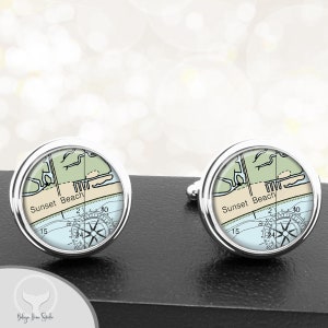 May include: A pair of silver cufflinks with a nautical map design. The map features a compass rose and the text "Sunset Beach".