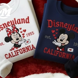 two Disney-themed sweatshirts, one white and one blue, with the text "Disneyland" and "California" printed on them.