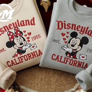 Two sweatshirts with the Disney theme park logo and text, featuring Minnie Mouse and Mickey Mouse.