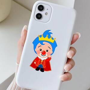 May include: White phone case with a cartoon clown prince illustration. The clown has blue hair, a red nose, and a gold crown, and is wearing a red cape. The phone case has a dual-camera setup.