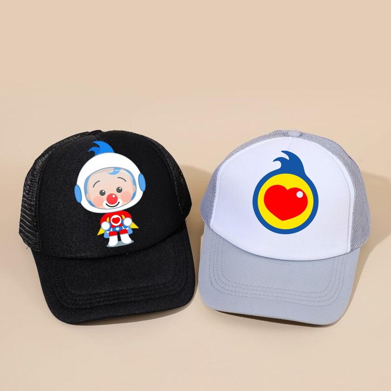May include: Two baseball caps. One is black with a cartoon astronaut graphic. The other is grey and white with a heart-shaped design inside a yellow circle. Both caps have a mesh back and a curved peak.