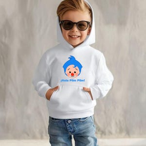 May include: White hooded sweatshirt with a cartoon character design, blue hair, a red nose, and the text "&iexcl;Hola Plim Plim!" in blue. The sweatshirt has a front pocket and is worn by a child wearing sunglasses and blue jeans.