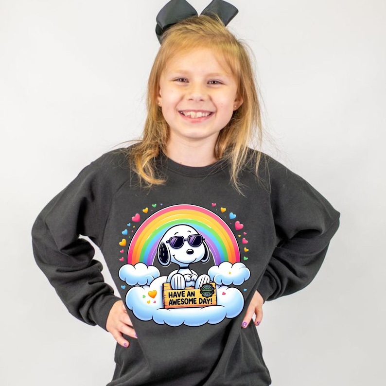 May include: A black sweatshirt featuring a colorful rainbow and a cartoon dog wearing sunglasses. The dog is sitting on a cloud and holding a sign that says "Have an Awesome Day!" The design is surrounded by hearts.