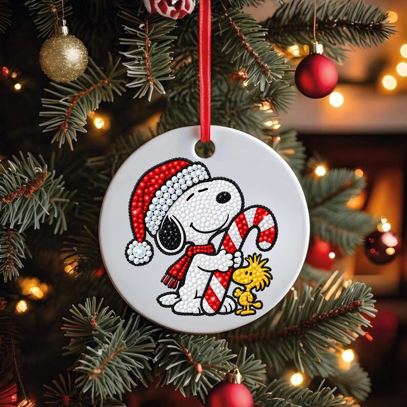 May include: A round white ceramic Christmas ornament featuring a diamond art design of a white dog wearing a red Santa hat and scarf, holding a red and white candy cane, with a small yellow bird standing beside it, hung by a red ribbon.