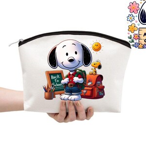 May include: A white canvas cosmetic bag with a black zipper, held by a hand. The bag features a colorful illustration of Snoopy with a backpack, a school bag, and the text "Back to School". A smiling sun and Woodstock are also depicted.