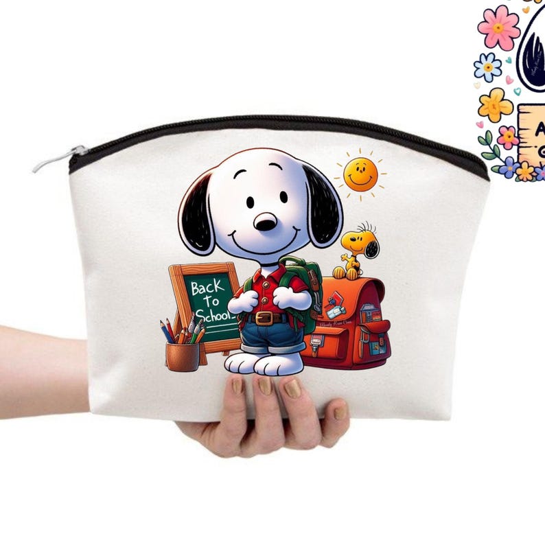 May include: A white canvas cosmetic bag with a black zipper, held by a hand. The bag features a colorful illustration of Snoopy with a backpack, a school bag, and the text "Back to School". A smiling sun and Woodstock are also depicted.