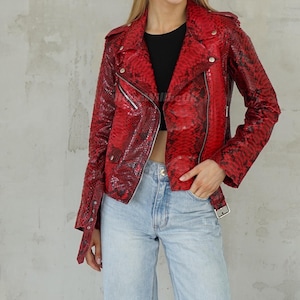 Op de afbeelding: Rode leren jas met slangenpatroon in klassieke bikerstijl. De jas heeft een reverskraag, een asymmetrische rits en zilverkleurige hardware. De mouwen hebben ritsen bij de manchetten en de jas heeft een riem in de taille.