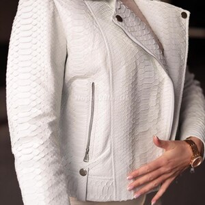Puede incluir: Chaqueta de cuero blanca con estampado de piel de serpiente. La chaqueta tiene cuello con solapas, cierre de cremallera y un peque&ntilde;o bolsillo con cremallera en el pecho. La chaqueta tiene un corte entallado y detalles plateados.