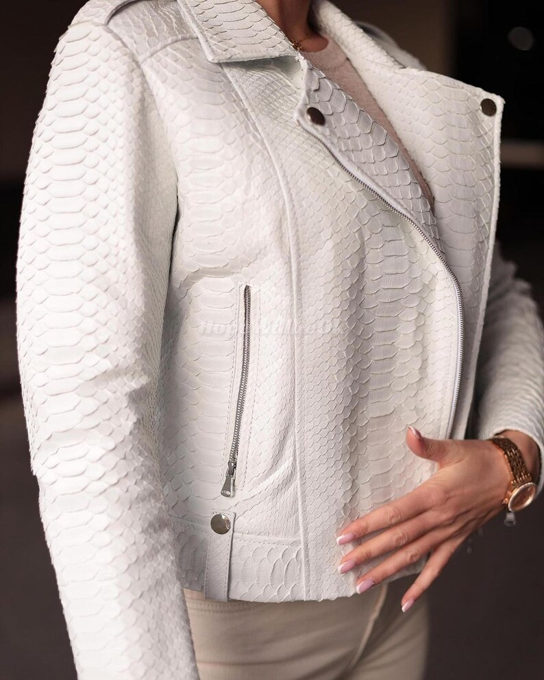 Puede incluir: Chaqueta de cuero blanca con estampado de piel de serpiente. La chaqueta tiene cuello con solapas, cierre de cremallera y un peque&ntilde;o bolsillo con cremallera en el pecho. La chaqueta tiene un corte entallado y detalles plateados.