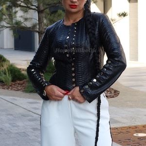 May include: A black textured jacket with gold buttons and long sleeves. The jacket has a round collar and is fastened with buttons. The text "HopeWillbeOk" is visible. The jacket is worn with white trousers.