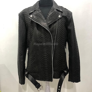 Könnte beinhalten: Schwarze Leder-Bikerjacke mit Schlangenleder-Textur. Die Jacke hat einen Reverskragen, einen asymmetrischen Reißverschluss und einen Gürtel in der Taille. Die Ärmel haben Reißverschlüsse an den Manschetten. Die Jacke wird auf einer Schaufensterpuppe präsentiert.
