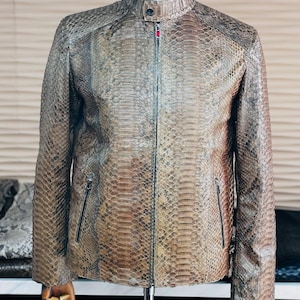 May include: A brown leather jacket with a snakeskin pattern. The jacket has a stand-up collar, a full-length zipper, and two zippered pockets. The jacket is displayed on a mannequin.