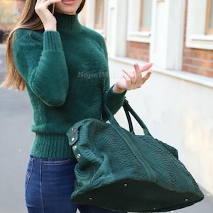 Puede incluir: Un suéter de cuello alto verde oscuro con textura difusa, puños y dobladillo acanalados, combinado con jeans azul oscuro y un bolso grande de color verde oscuro con textura de piel de serpiente, herrajes metálicos plateados y cierre de cremallera.