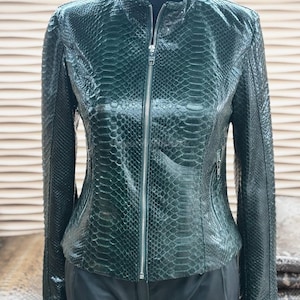 May include: Dark green leather jacket with a snakeskin pattern. The jacket features a stand-up collar, a full-length zip, and two zipped pockets. The jacket is displayed on a mannequin.