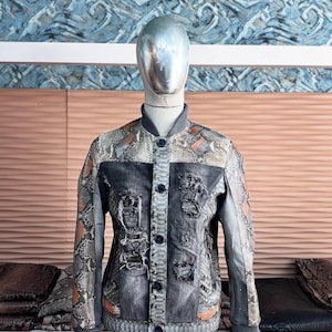 May include: A distinctive jacket with a snakeskin design and denim detailing. The jacket combines grey, brown, and orange hues, with a button closure and ribbed cuffs. The design incorporates distressed denim patches.