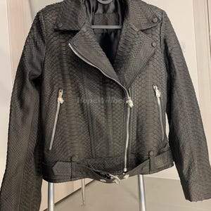 May include: Black leather jacket with a snakeskin pattern. The jacket features a classic biker style with a notched collar, asymmetrical zipper closure, and a belt at the waist. Silver zippers and hardware add a contrasting detail to the jacket.