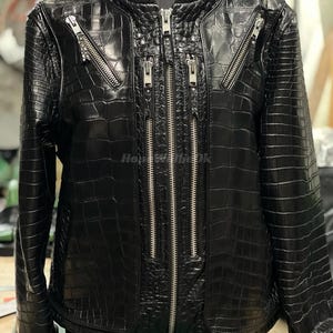 May include: A black leather jacket with a crocodile skin texture. The jacket features multiple silver zippers and a ribbed collar and cuffs. The jacket is displayed on a mannequin.