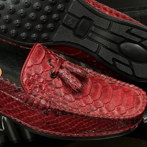 Op de afbeelding: Rode leren loafers met een getextureerd, geschubd patroon. De schoenen hebben een ronde neus, een kwastdetail en een zwarte rubberen zool. De zool heeft een gestructureerd ontwerp voor grip.