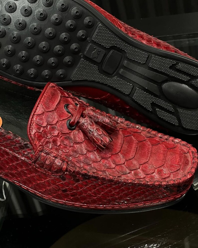 Op de afbeelding: Rode leren loafers met een getextureerd, geschubd patroon. De schoenen hebben een ronde neus, een kwastdetail en een zwarte rubberen zool. De zool heeft een gestructureerd ontwerp voor grip.