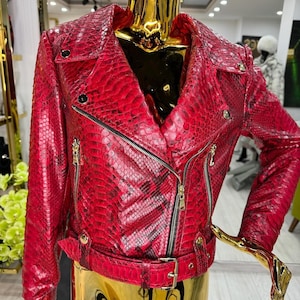 May include: A red snakeskin-textured leather jacket with a classic biker style. The jacket features a notched collar, asymmetrical zipper closure, and a belted waist. Gold-toned hardware accents the jacket, including zippers and belt buckle.