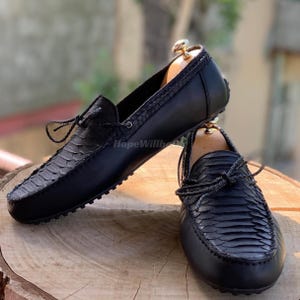 May include: A pair of black leather loafers with a snakeskin pattern on the vamp. The shoes have a classic design with a rounded toe and a leather tie detail. The soles are black with a rubber grip.