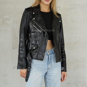 May include: A black snakeskin-patterned leather jacket. The biker-style jacket features a notched collar, an off-centre zip, and silver-coloured hardware. It is worn with a black top and light blue jeans.