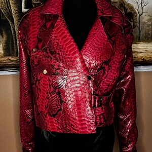 Può includere: Giacca rossa con motivo a pelle di serpente, in classico stile biker. La giacca presenta un colletto a revers, una zip asimmetrica e una cintura in vita. Ha due tasche frontali e bottoni color oro.