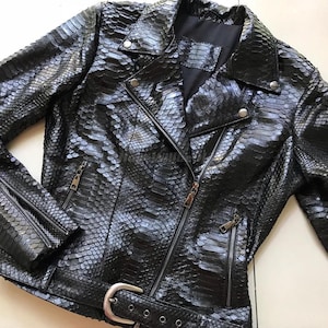 以下が含まれることがあります： 黒いヘビ革模様のレザージャケット。クラシックなバイカースタイル。ノッチカラー、非対称ジッパー開閉、複数のジッパーポケット、ウエストベルトが特徴です。ジャケットはシルバーの金具とテクスチャード加工が施されています。