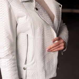 Puede incluir: Chaqueta de cuero blanca con estampado de piel de serpiente. La chaqueta tiene cuello con solapas, cierre de cremallera y un peque&ntilde;o bolsillo con cremallera en el pecho. La chaqueta tiene un corte entallado y es una opci&oacute;n de abrigo elegante.