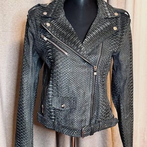 May include: A dark grey faux leather jacket with a snakeskin pattern. The jacket has a classic biker style with an asymmetrical zip, notched lapels, and a belted waist. Silver-tone hardware accents the design.