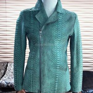 Può includere: Giacca in pelle color verde acqua con motivo a pelle di serpente. La giacca presenta una chiusura con cerniera, un colletto a revers e maniche lunghe. La giacca è esposta su un manichino.
