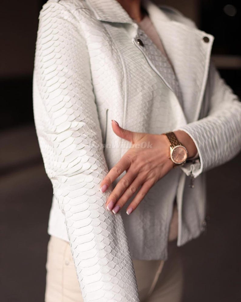 Puede incluir: Chaqueta de cuero blanca texturizada con un patr&oacute;n de piel de serpiente. La chaqueta tiene un cuello cl&aacute;sico, cierre de cremallera y mangas largas. Se ve un reloj dorado en la mu&ntilde;eca. Prenda de vestir exterior elegante.