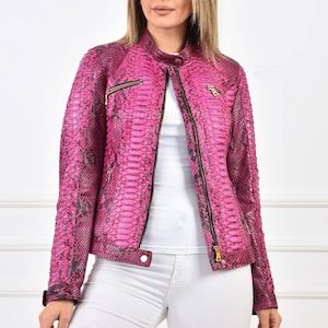 May include: A bright pink leather jacket with a snakeskin design. The jacket has a stand-up collar, a front zip, and gold-coloured hardware. The sleeves have zips at the cuffs. The jacket is a striking fashion piece.