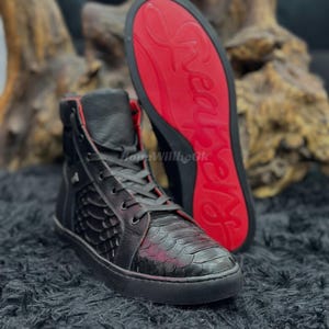 May include: Black high-top sneakers with red accents and soles. The sneakers feature a textured pattern on the sides and a lace-up closure. The red soles have a brand name in white.