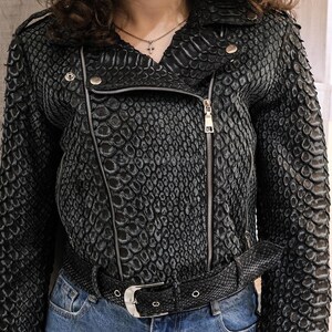 Può includere: Giacca da motociclista nera in ecopelle effetto serpente con cerniere e hardware argentati. La giacca presenta un colletto a revers, una chiusura asimmetrica con zip e una cintura abbinata. Il motivo strutturato conferisce alla giacca un aspetto unico.