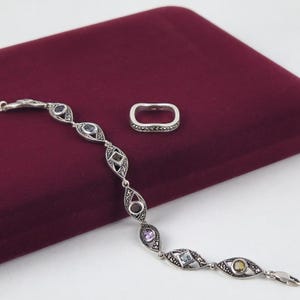 May include: A silver bracelet featuring marquise-shaped links with marcasite accents and various multi-colored gemstones, accompanied by a matching rectangular silver ring with a marcasite-encrusted band and a smooth, polished silver center.