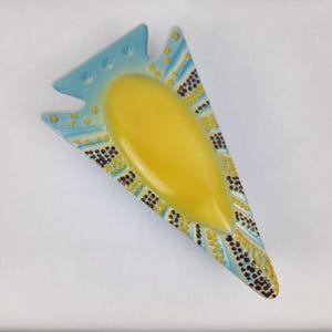 May include: A unique, mid-century modern ashtray in a triangular shape. The ashtray features a bright yellow center and is bordered by a light blue and white design with brown and yellow accents. The ashtray is made of ceramic.