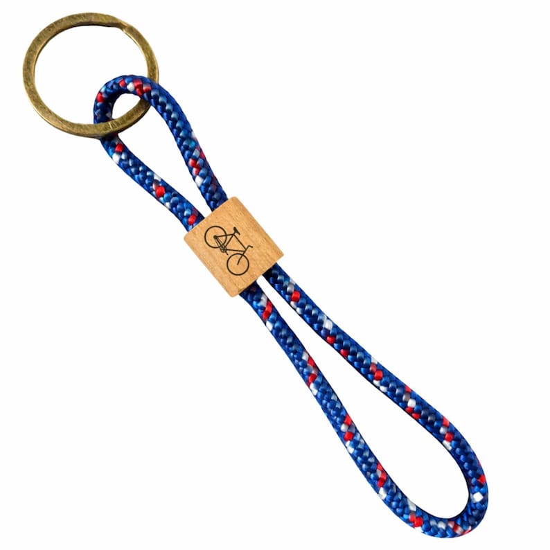 May include: A blue, red, and white rope keychain with a wooden accent featuring a bicycle graphic. The keychain has a brass-colored ring for attaching keys.